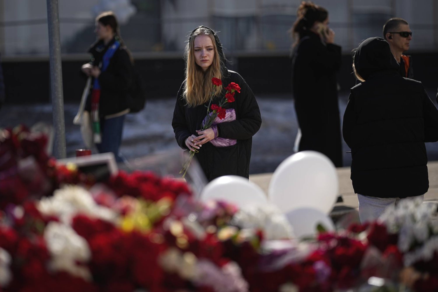 شابة تحمل أزهار القرنفل الحمراء أمام نصب تذكاري أمام قاعة مدينة كروكوس في الضواحي الغربية لموسكو حيث وقع هجوم دامٍ على قاعة الحفلات الموسيقية الأسبوع الماضي (أ.ب)