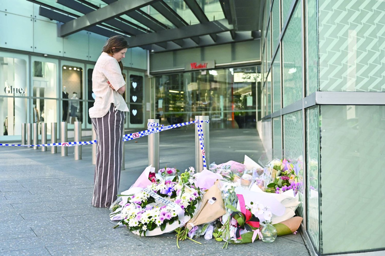 
أسترالية تنظر إلى زهور تركها مواطنون أمس تحيةً لضحايا الهجوم الذي حدث عند مدخل مركز تسوق في سيدني (أ.ب)