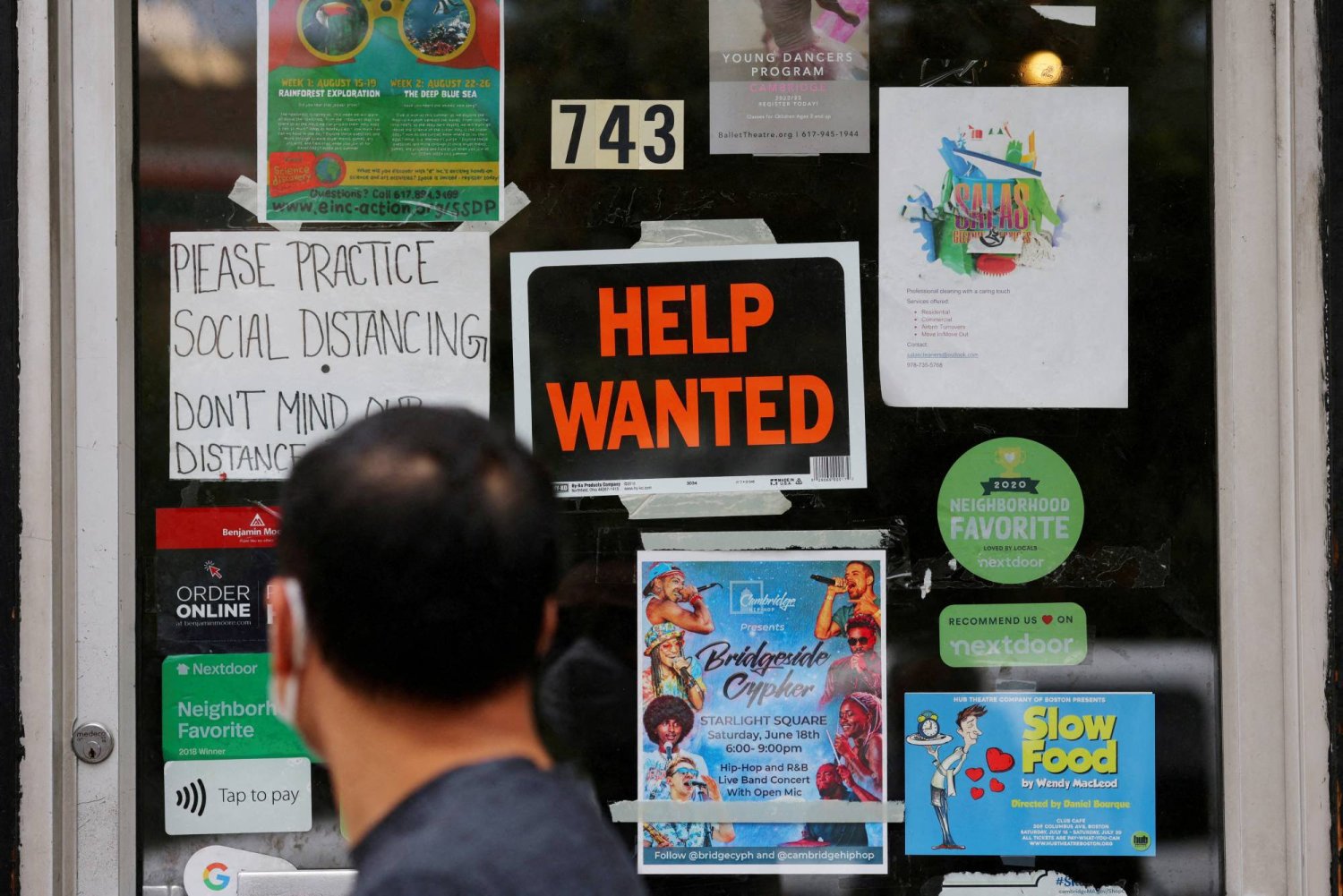 أحد المشاة يمر بالقرب من لافتة «مطلوب مساعدة» على باب متجر لأجهزة الكومبيوتر في كامبريدج بالولايات المتحدة (رويترز)
