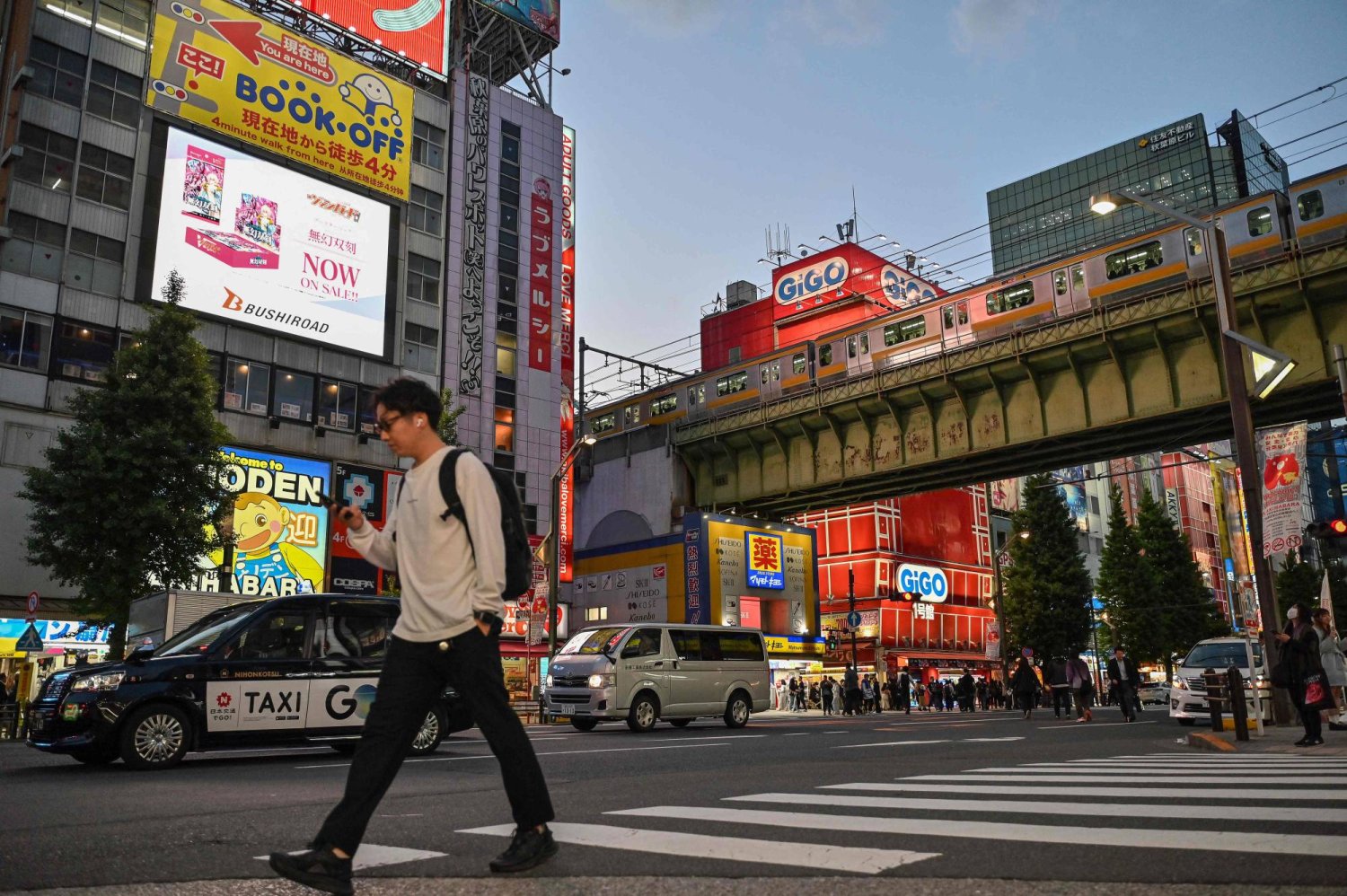 رجل يعبر الطريق أمام محطة قطارات في إحدى ضواحي العاصمة اليابانية طوكيو (أ.ف.ب)
