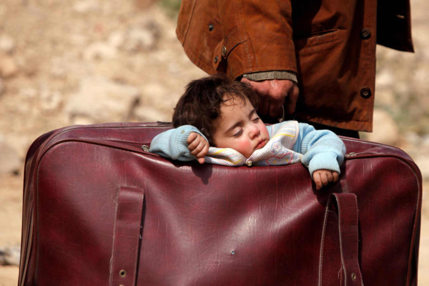 طفل سوري نازح ينام في حقيبة سفر بقرية بيت سوا في الغوطة الشرقية (رويترز)