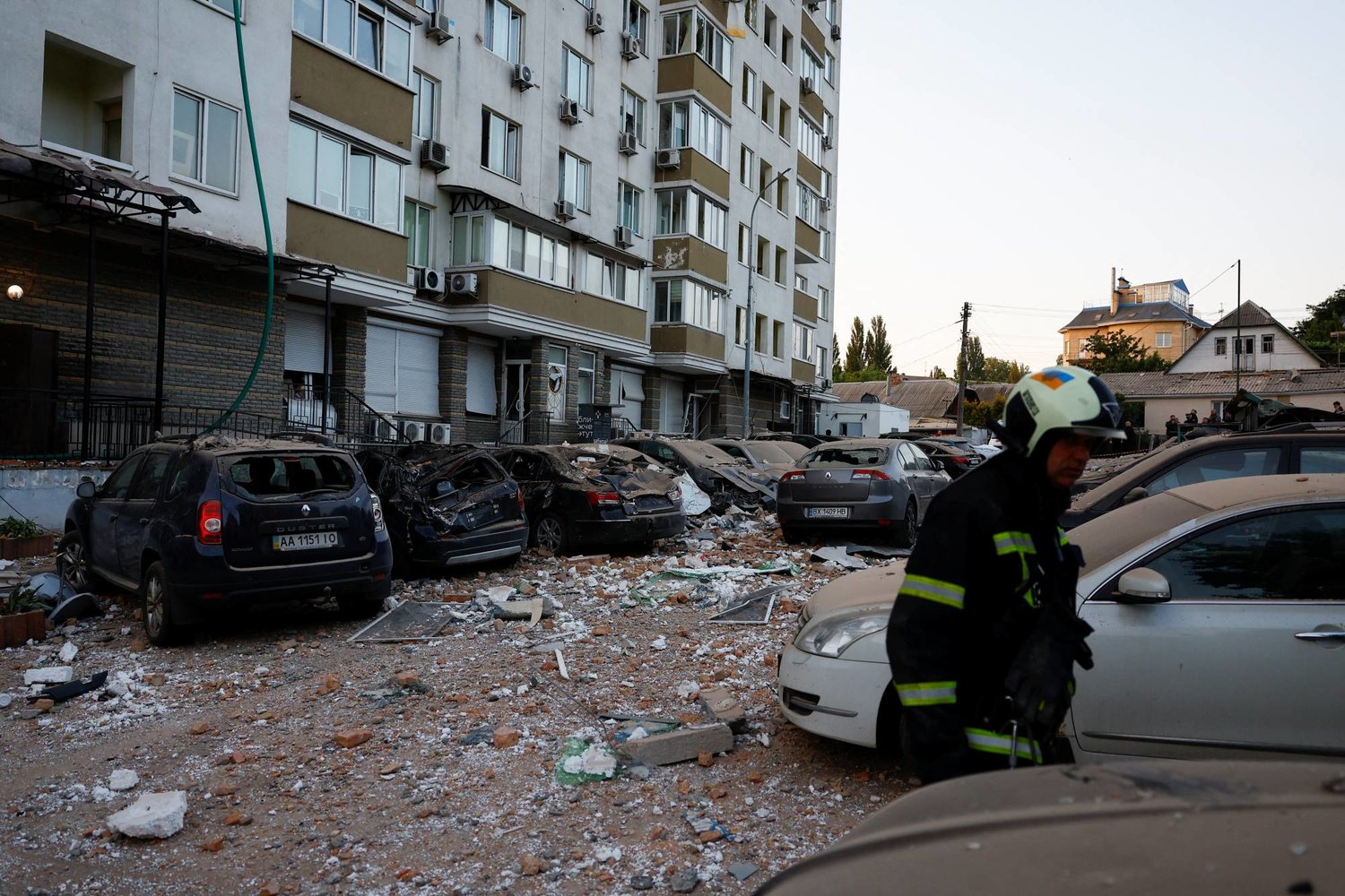 رجال إطفاء أمام مبنى وسيارات متضررة من الهجوم الروسي على كييف (رويترز)