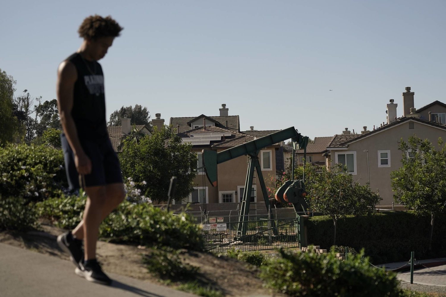 شاب يسير في شارع وبجانبه حفارة تعمل بموقع حفر للنفط بجوار المنازل بكاليفورنيا (أ.ب)