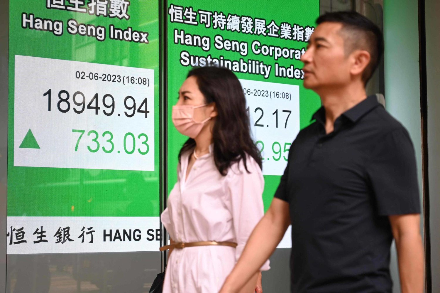 رجل وامرأة يسيران أمام شاشة تعرض مؤشر هانغ سينغ الرئيسي في بورصة هونغ كونغ (أ ف ب)