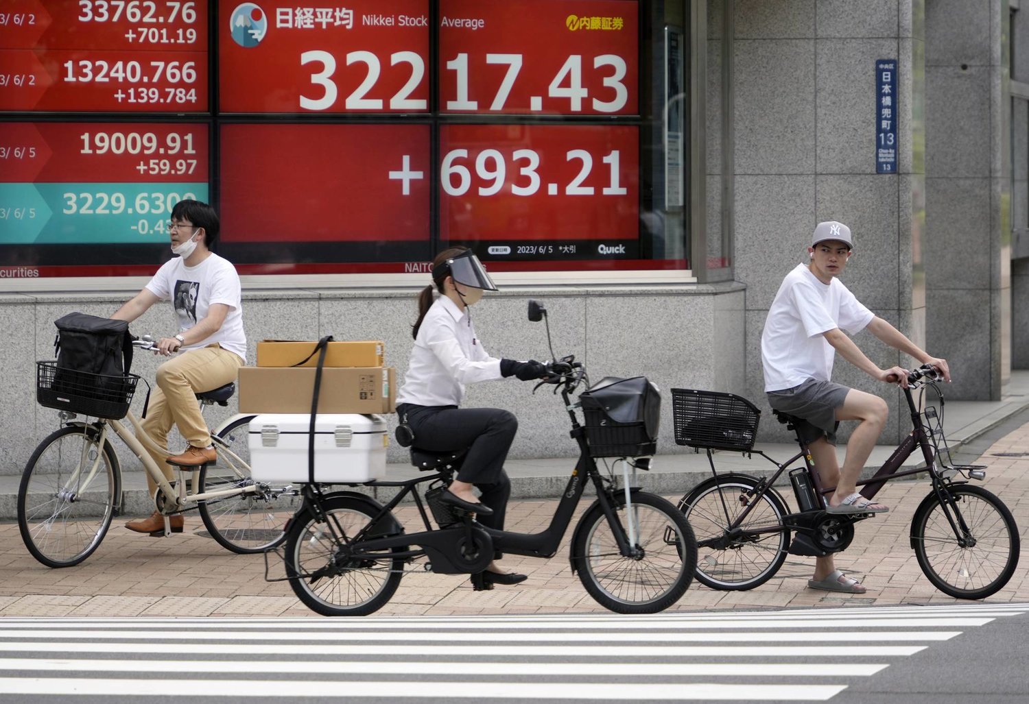 دراجون يمرون وسط العاصمة اليابانية طوكيو أمام شاشة تعرض حركة الأسهم على مؤشر نيكي الذي حقق أعلى إغلاق في 33 عاماً (إ.ب.أ)