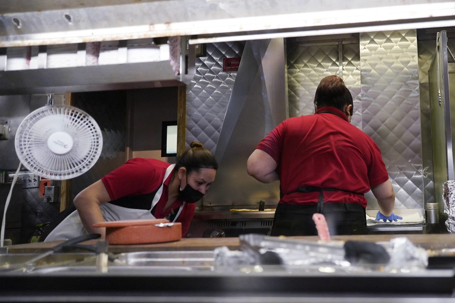 رجل وامرأة يعملان في مطبخ أحد مطاعم مدينة شيكاغو الأميركية بينما شهد قطاع الخدمات استقراراً يدعم مكافحة التضخم (أ.ب)
