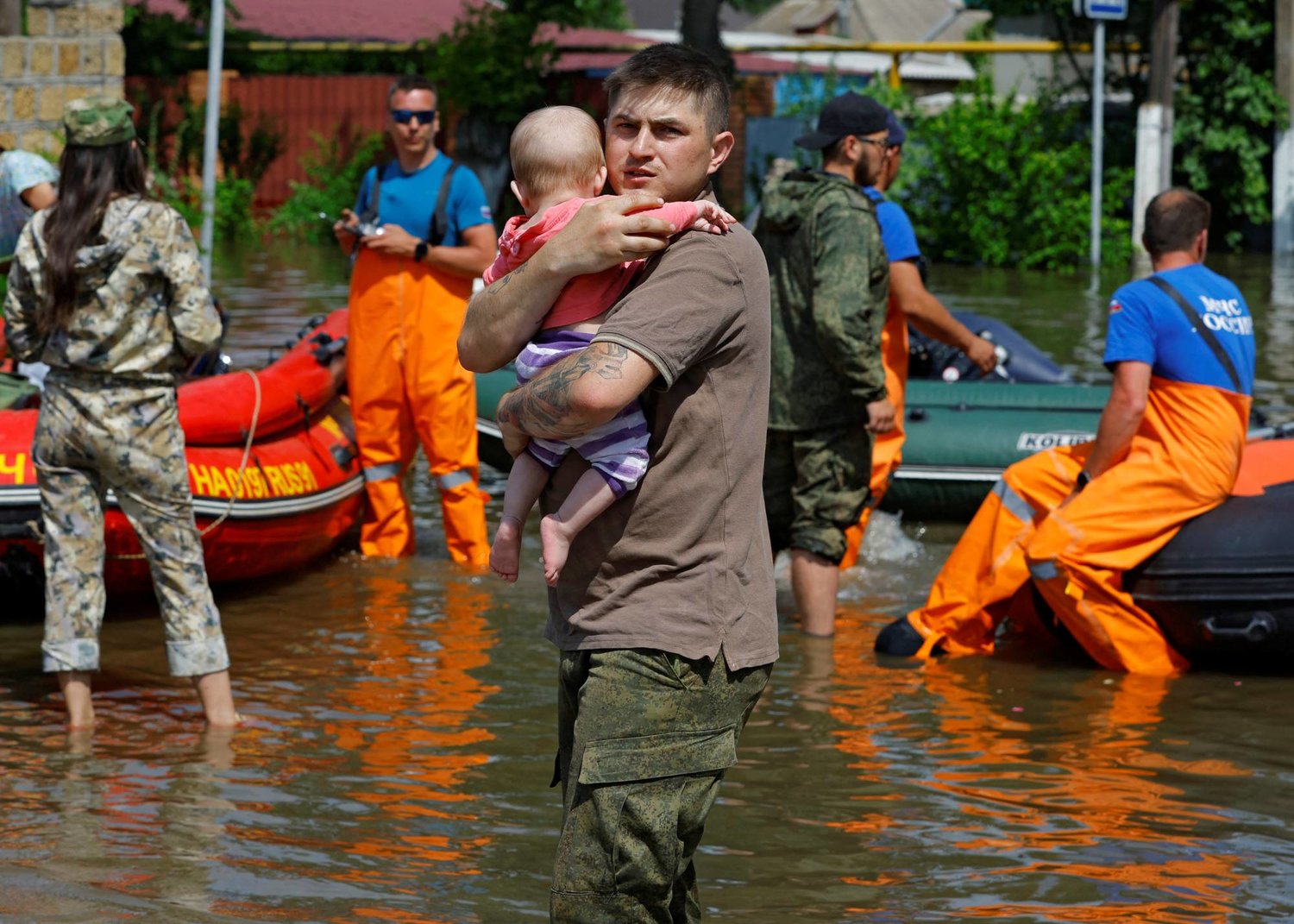 رجل يحمل طفلاً أثناء إجلاء أعضاء وزارة الطوارئ الروسية لسكان منطقة غمرتها الفيضانات عقب انهيار سد نوفا كاخوفكا (رويترز)