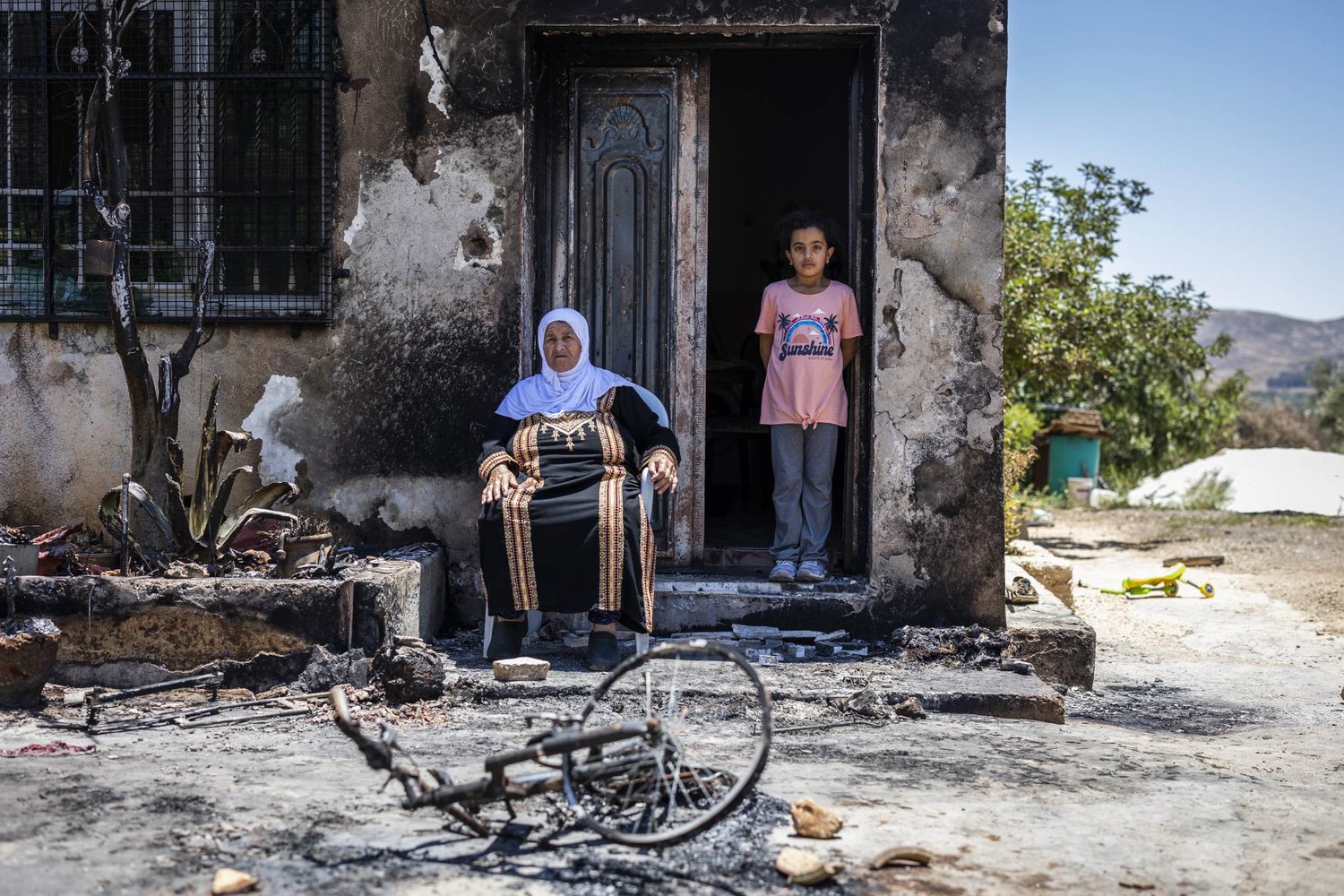 فلسطينيتان خارج منزلهما الذي أحرقه مستوطنون في 23 يونيو 2023 (د.ب.أ)