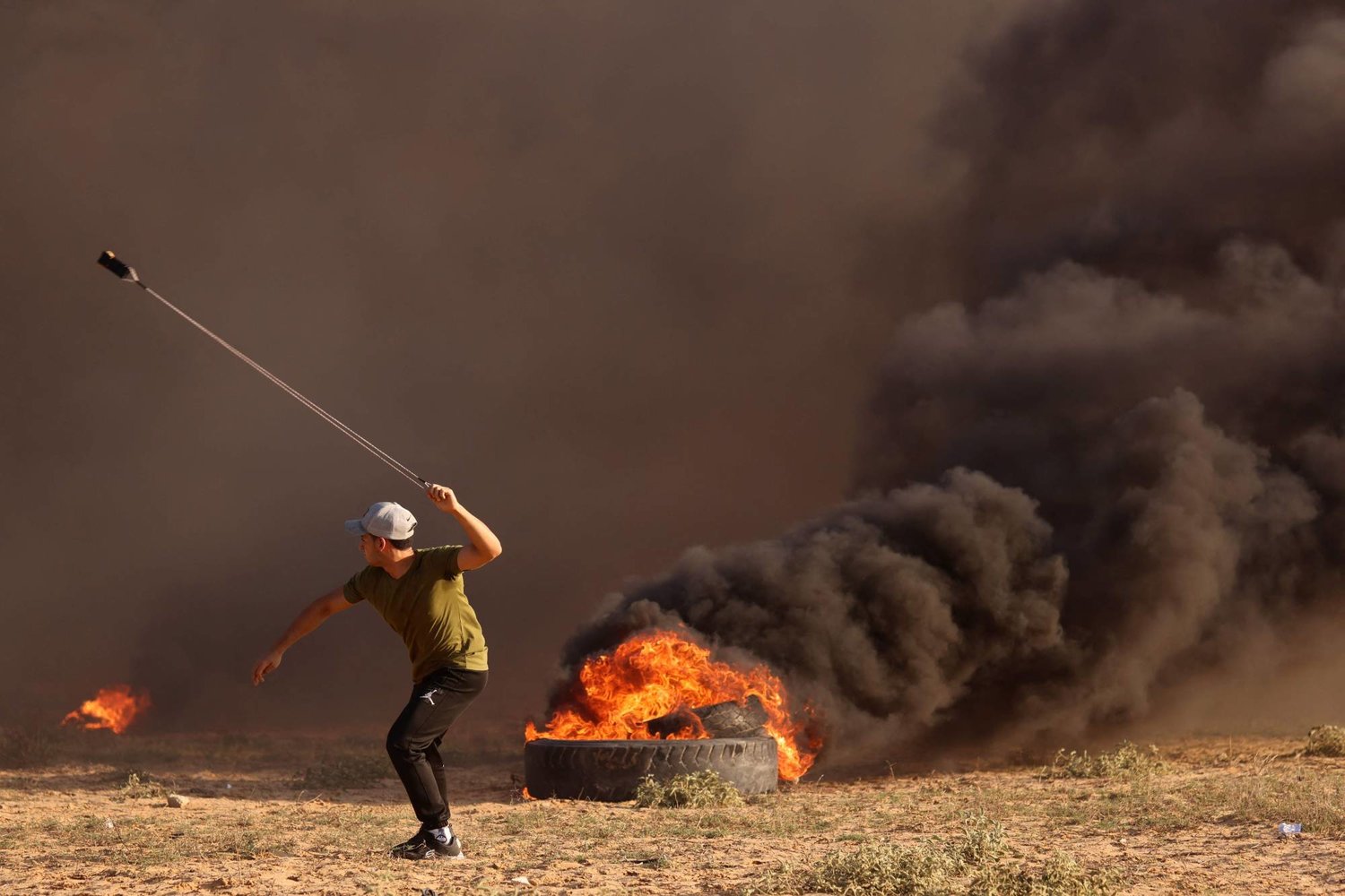 متظاهر فلسطيني يقذف أحجاراً على القوات الإسرائيلية شرق غزة وسط الإطارات المشتعلة (أ.ف.ب)