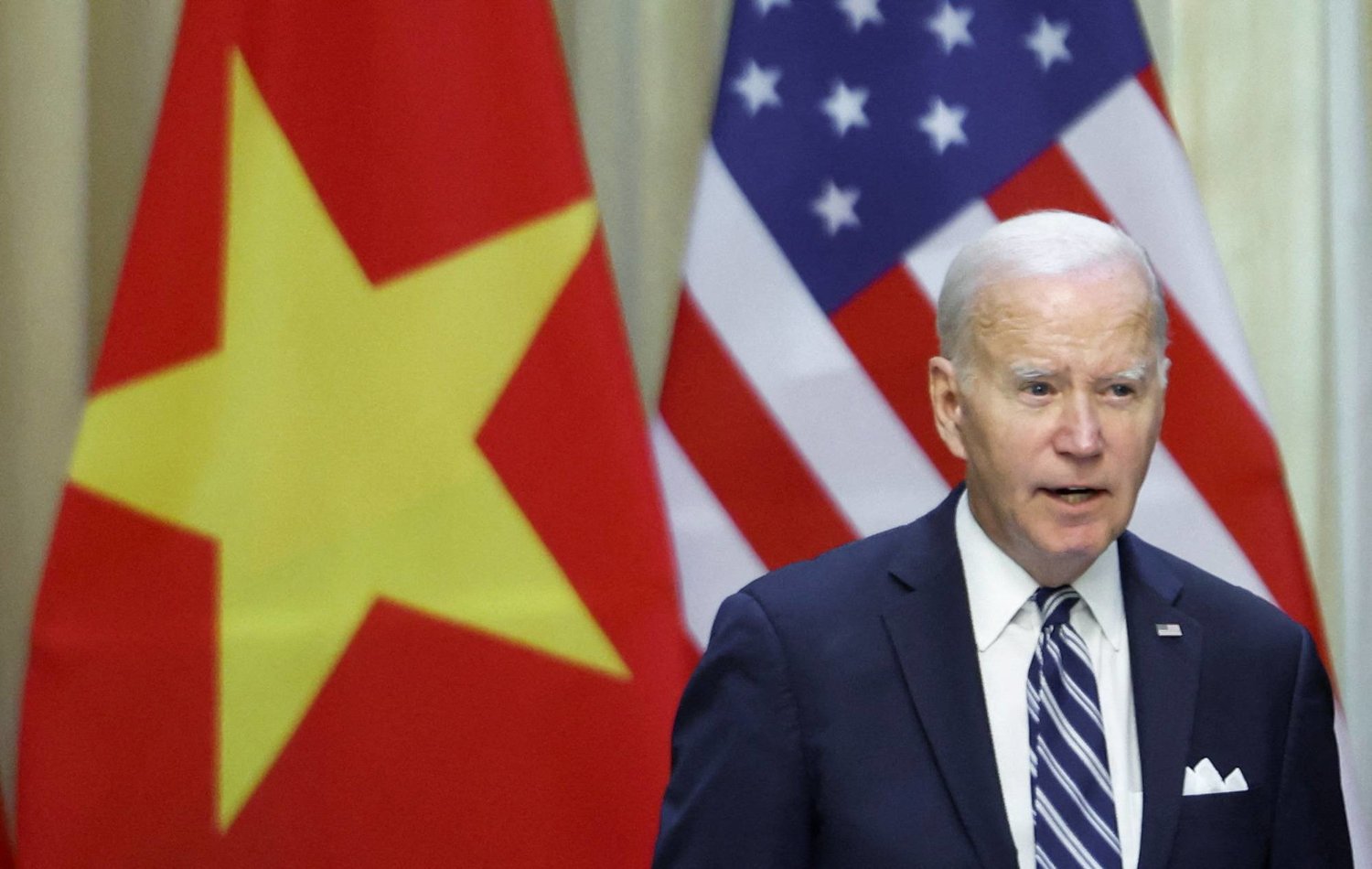 الرئيس الأميركي جو بايدن وخلفة علما أميركا وفيتنام (رويترز)