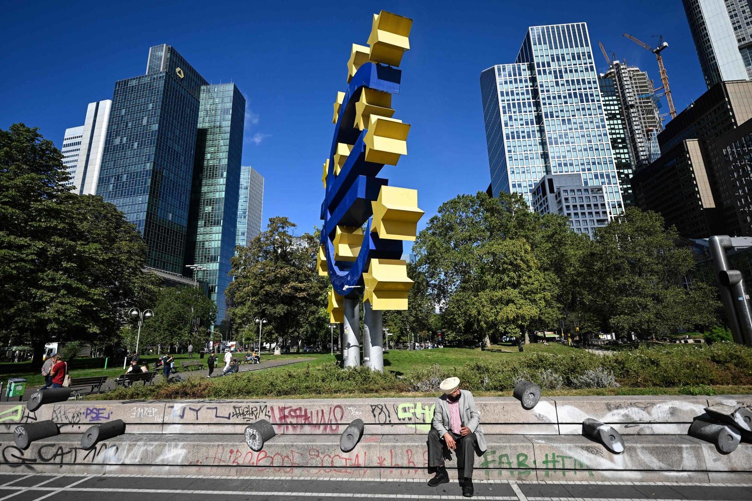 رجل يجلس أمام علامة عملة اليورو أمام مبنى «البنك المركزي الأوروبي» السابق (وكالة الصحافة الفرنسية)