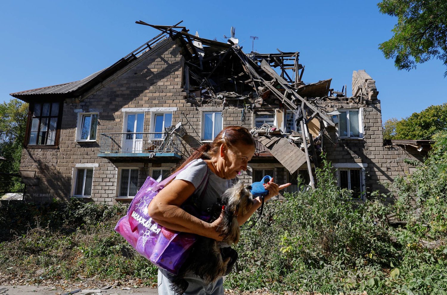تحمل كلبها معها أمام منزل متضرر بفعل القتال في إقليم دونيتسك اليوم الأربعاء (رويترز)