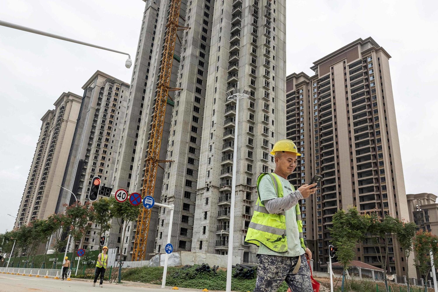 عامل يسير أمام أبراج في أحد مشروعات شركة «إيفرغراند» العقارية المتعثرة في مدينة ووهان الصينية (أ.ف.ب)
