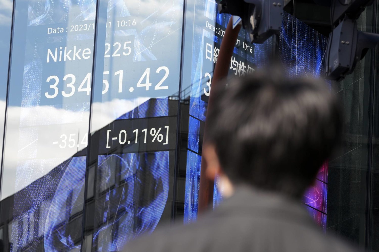 رجل ينظر من خلال الزجاج إلى شاشة إلكترونية تظهر تحركات الأسهم على مؤشر نيكي الياباني بالعاصمة طوكيو (أ.ب)