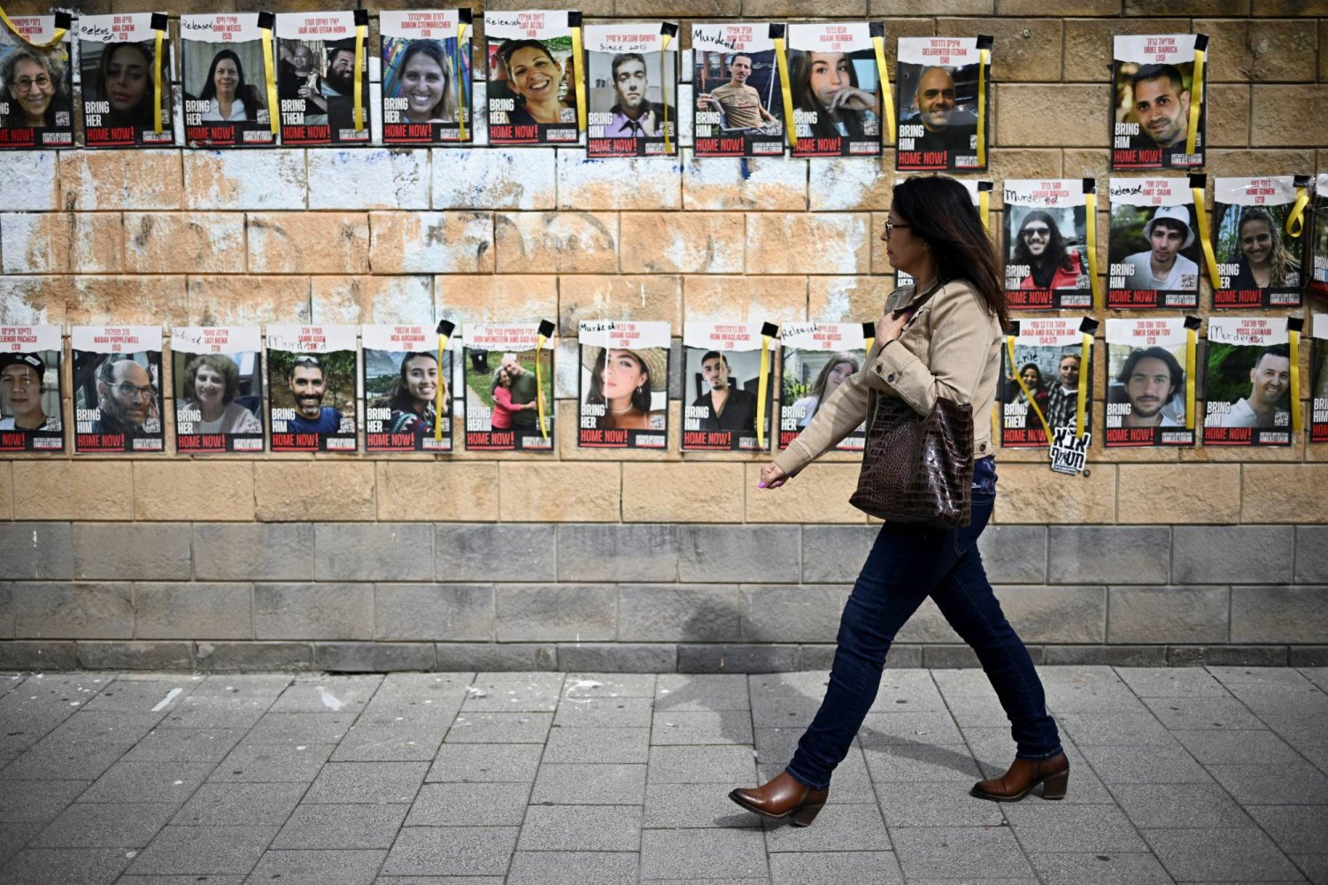 إسرائيلية تسير بجوار جدار عليه صور رهائن لدى «حماس» في تل أبيب الجمعة (رويترز)
