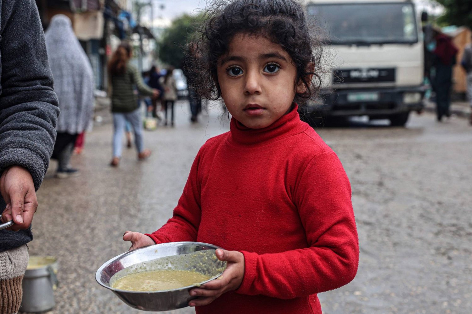 طفلة فلسطينية تحمل طبقاً من شوربة العدس قدّمه متطوعون في رفح (أ.ف.ب)