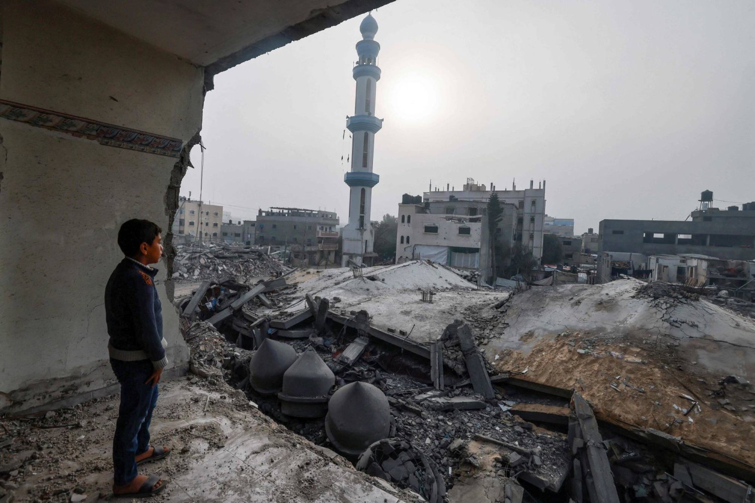 طفل فلسطيني داخل مبنى مدمر يطالع مسجداً طاله قصف إسرائيلي في رفح (أ.ف.ب) 