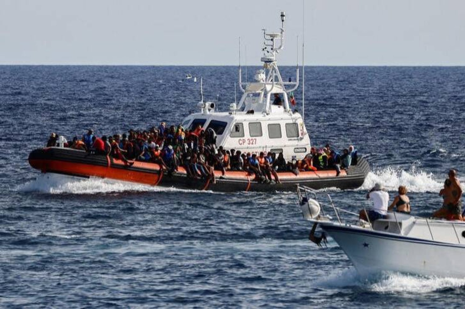 سفينة تابعة لخفر السواحل الإيطالي تحمل مهاجرين غير شرعيين تم إنقاذهم في البحر تمر بالقرب من قارب سياحي في جزيرة لامبيدوسا الصقلية بإيطاليا في 18 سبتمبر 2023 (رويترز)