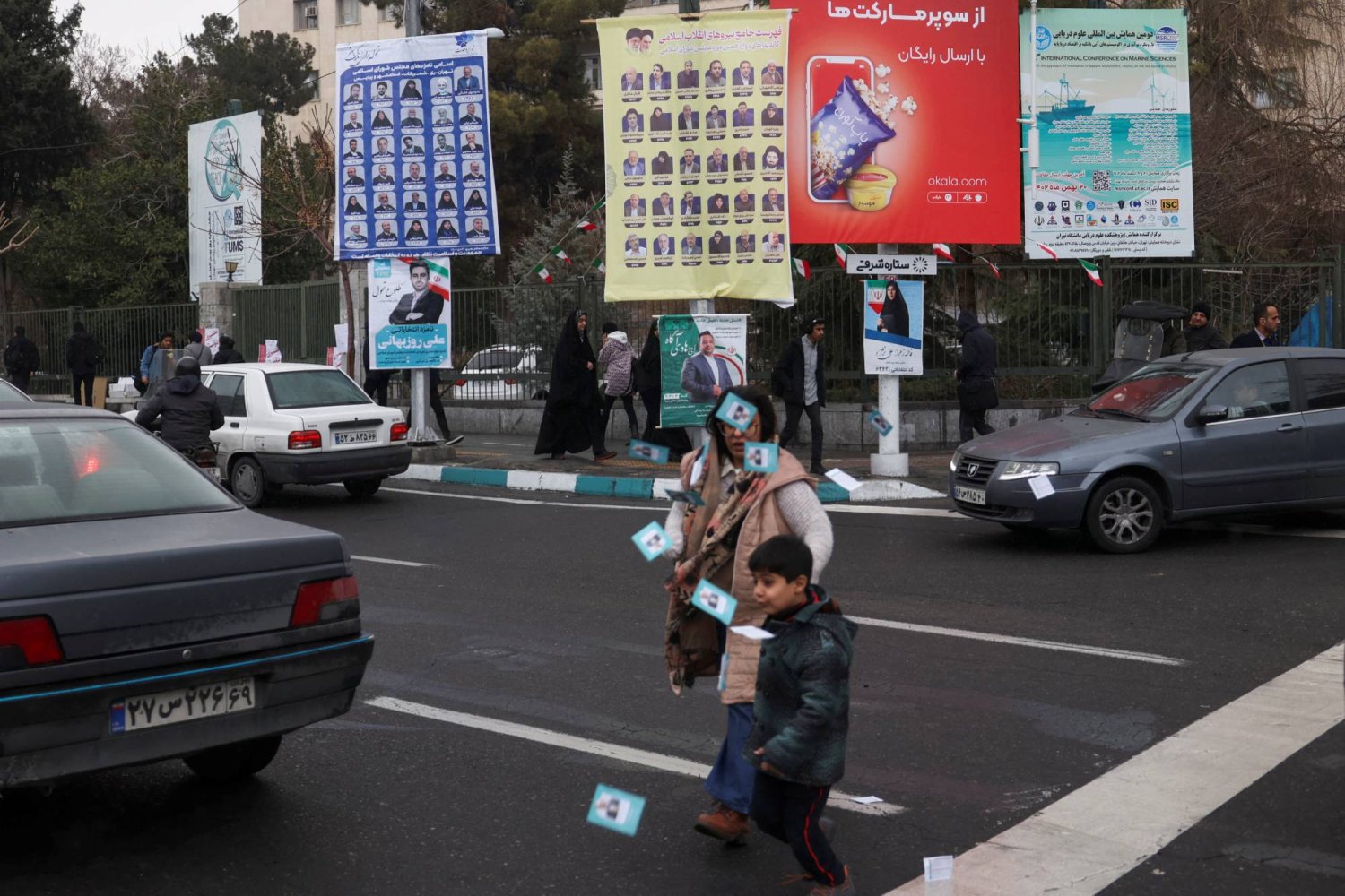 أشخاص يسيرون أمام ملصقات الحملة الانتخابية في طهران (رويترز)