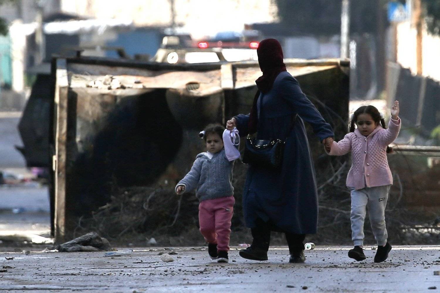 فلسطينية مع أطفالها تخرج من مخيم جنين للاجئين في وقت سابق متجهة إلى مكان أكثر أماناً (إ.ب.أ)