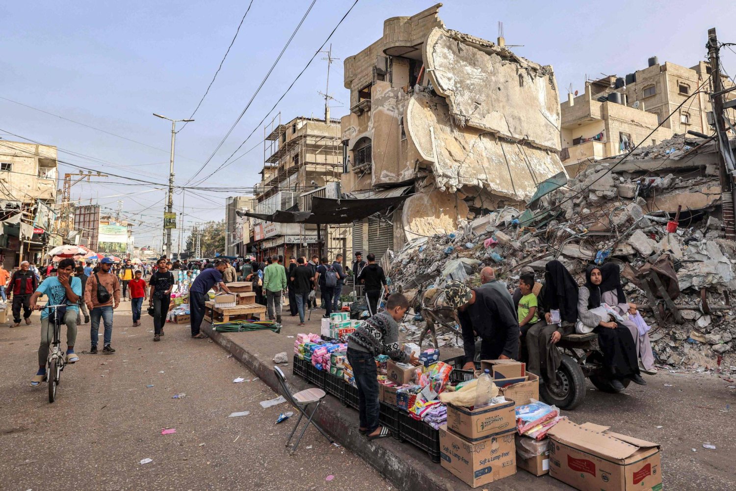 صبي يساعد بائعاً في ترتيب بضائعه خلال وقوفه أمام أنقاض مبنى منهار في رفح بجنوب قطاع غزة (أ.ف.ب)