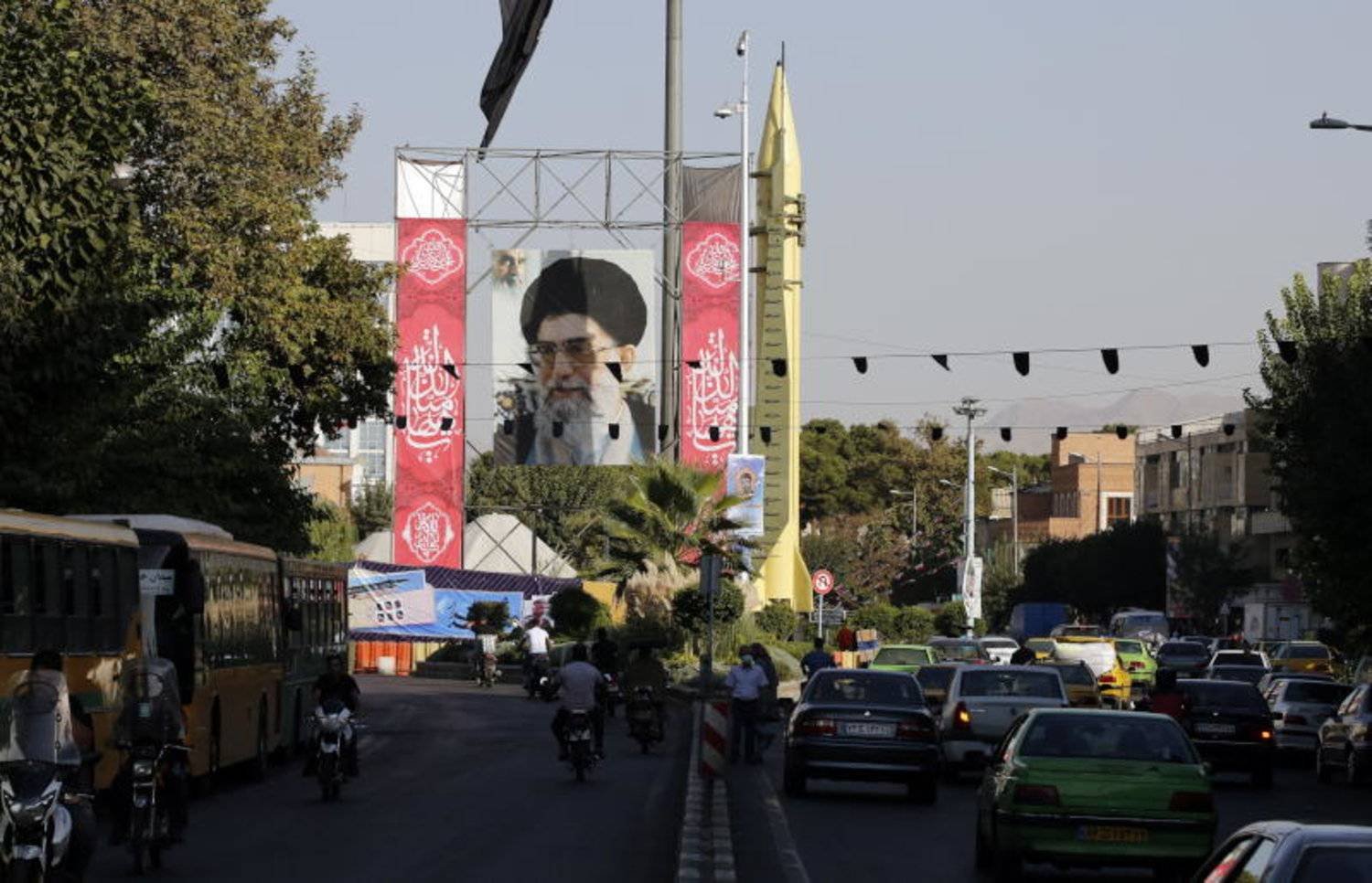 إيرانيون يمرون بجانب صاروخ «أرض- أرض» من طراز «شهاب 3» معروض بجوار صورة المرشد علي خامنئي في معرض بأحد شوارع طهران (إ.ب.أ)