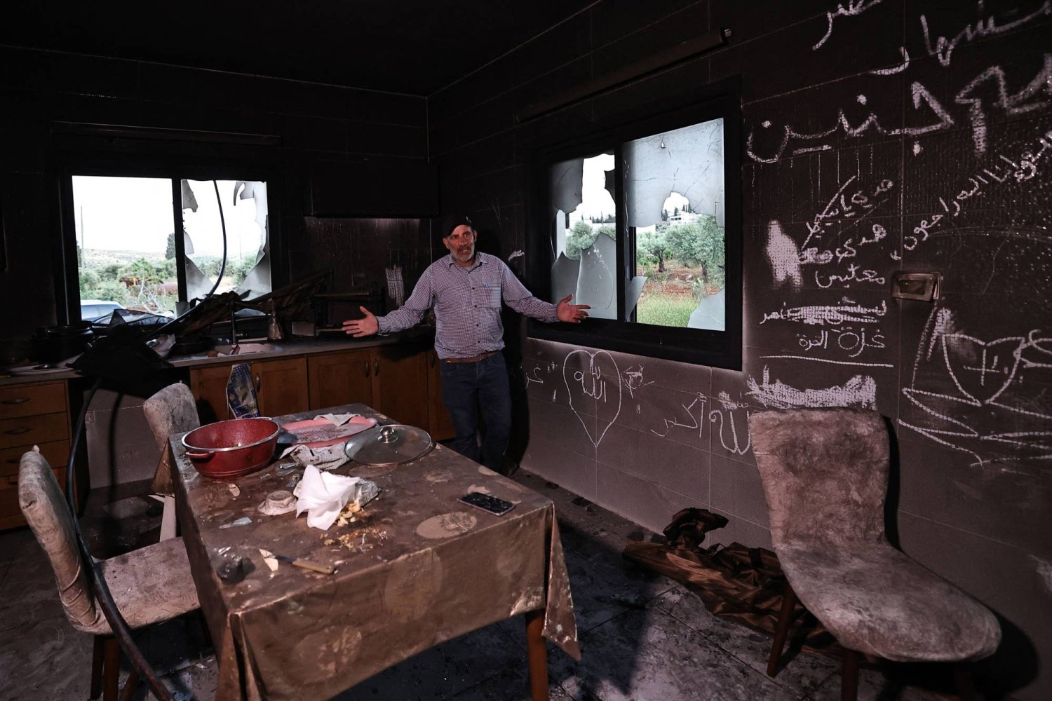 رجل فلسطيني يشير وهو يقف داخل مطبخه في أعقاب هجوم شنه مستوطنون إسرائيليون في قرية المغير بالضفة الغربية المحتلة بالقرب من رام الله (أ.ف.ب)
