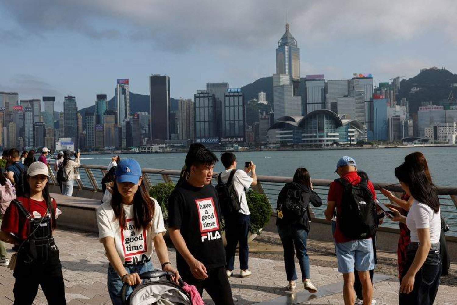 سياح صينيون من البر الرئيسي يسيرون أمام أفق المباني في تسيم شا تسوي بهونغ كونغ بالصين (رويترز)