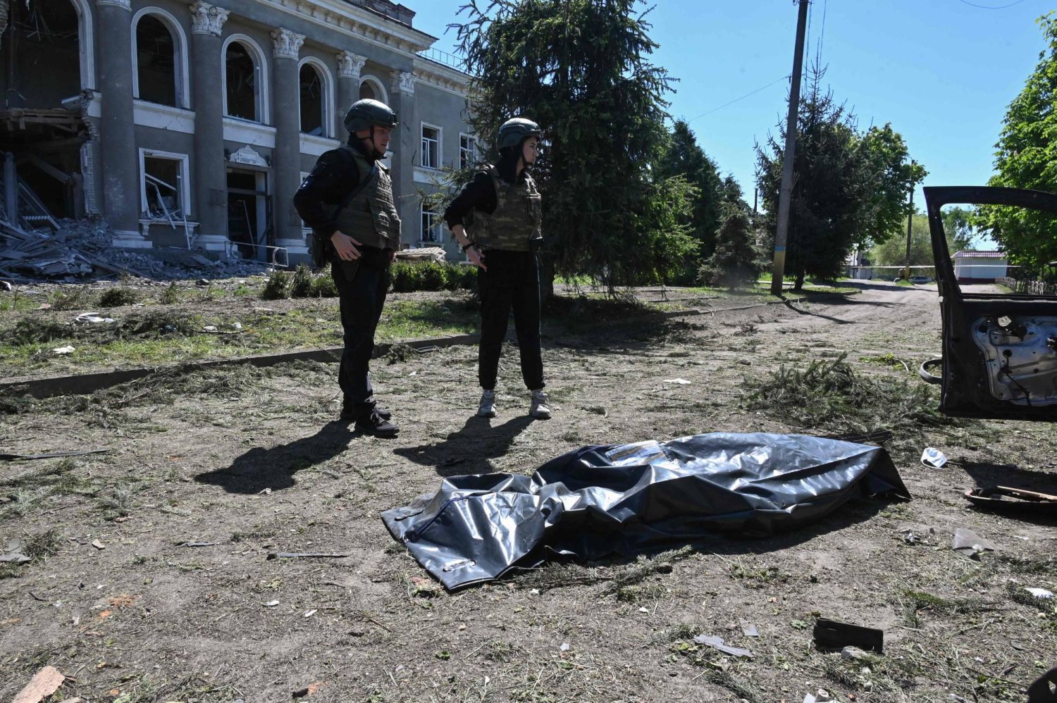 ضباط أوكرانيون يقفون بجوار جثة بعد غارة استهدفت قرية في منطقة خاركيف (ا.ف.ب)