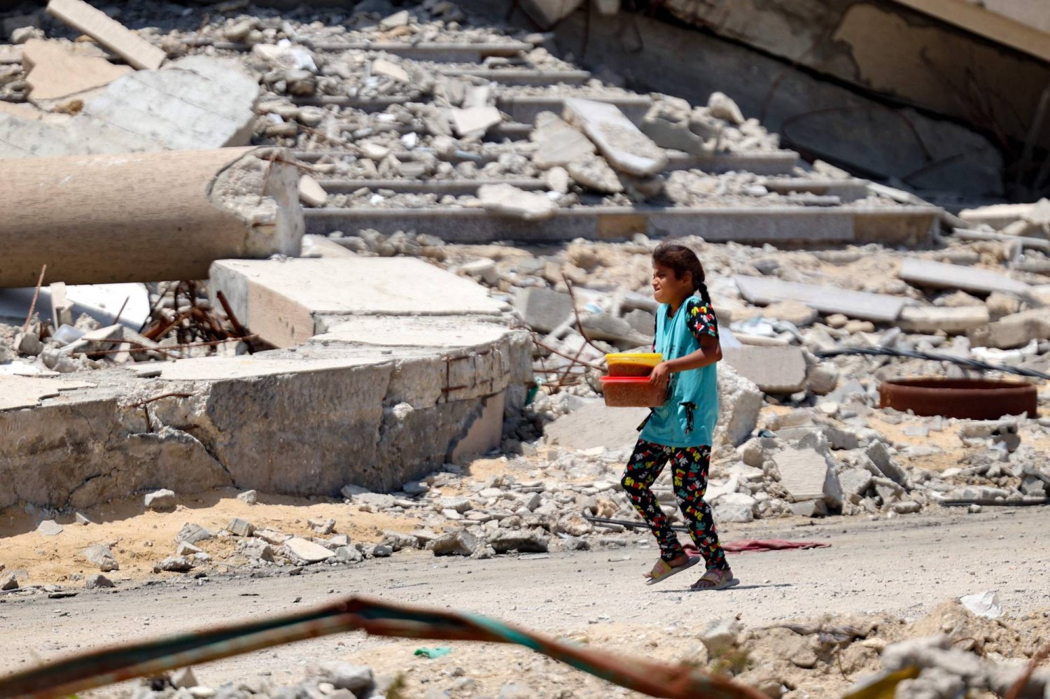 طفلة فلسطينية تحمل حصة من الطعام الذي يوزعه المطبخ الخيري وسط مشاهد الدمار في مدينة غزة (أ.ف.ب)