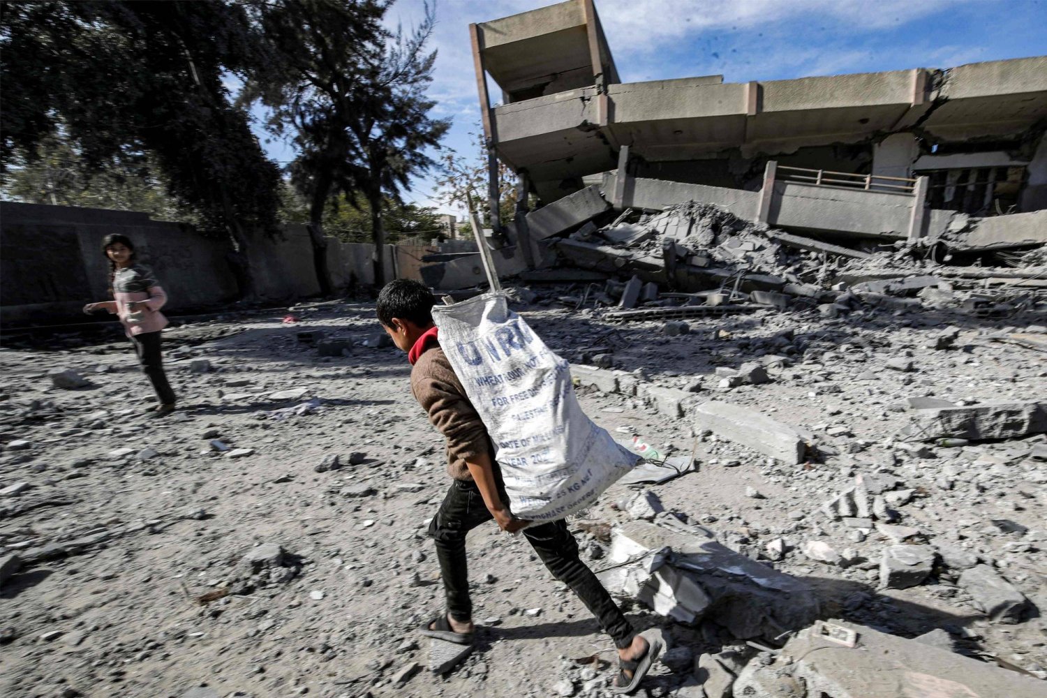 صبي يحمل كيساً مملوءاً بالمواد التي تم انتشالها من أنقاض مدرسة ثانوية مدمرة في مخيم النصيرات للاجئين الفلسطينيين (أ.ف.ب)