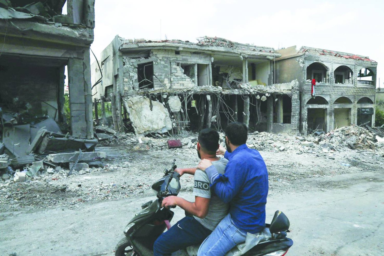 
رجلان على متن دراجة نارية يعاينان مباني متضررة بفعل غارة إسرائيلية في قرية ميس الجبل الحدودية بجنوب لبنان أمس (أ.ف.ب)