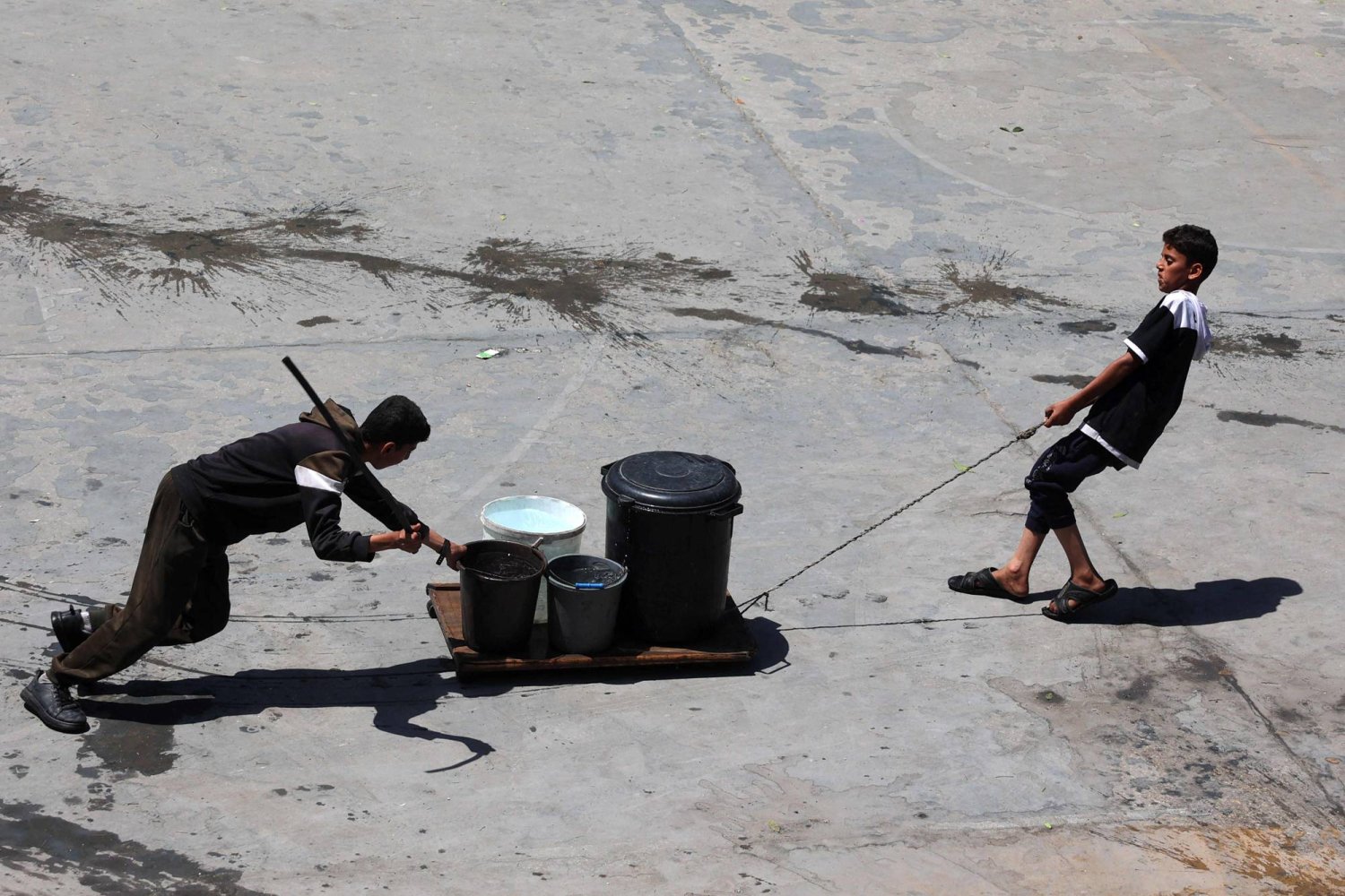 طفلان يجذبان قطعةً خشبيةً محملةً بالماء في ساحة مدرسة تديرها وكالة الأمم المتحدة (الأونروا) بمخيم الشاطئ للاجئين الفلسطينيين غرب مدينة غزة الثلاثاء (أ.ف.ب)