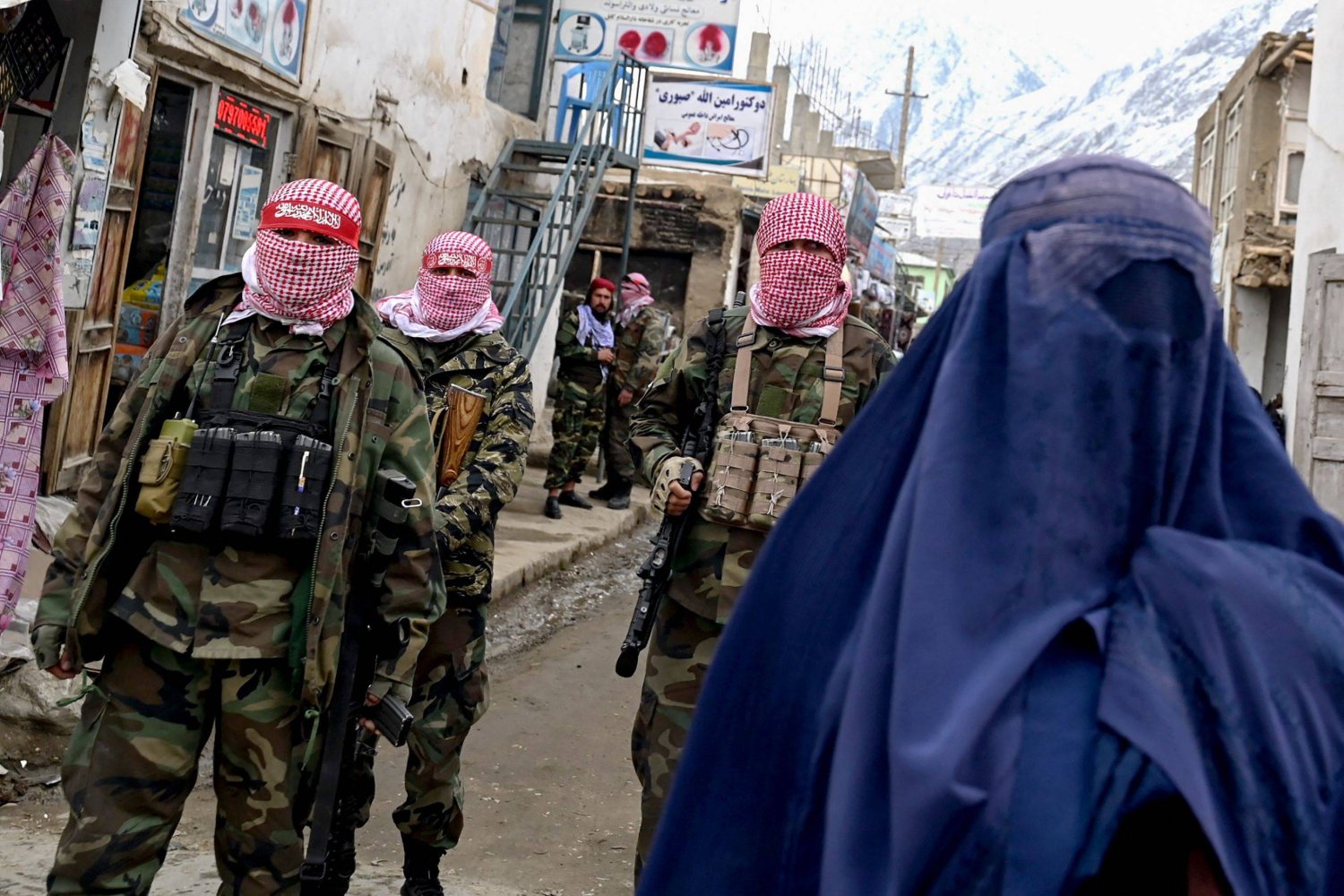 أفراد أمن «طالبان» يقفون للحراسة في حين تسير امرأة أفغانية ترتدي البرقع (على اليمين) على طول شارع في سوق في منطقة باهاراك بمقاطعة بدخشان (أ.ف.ب)