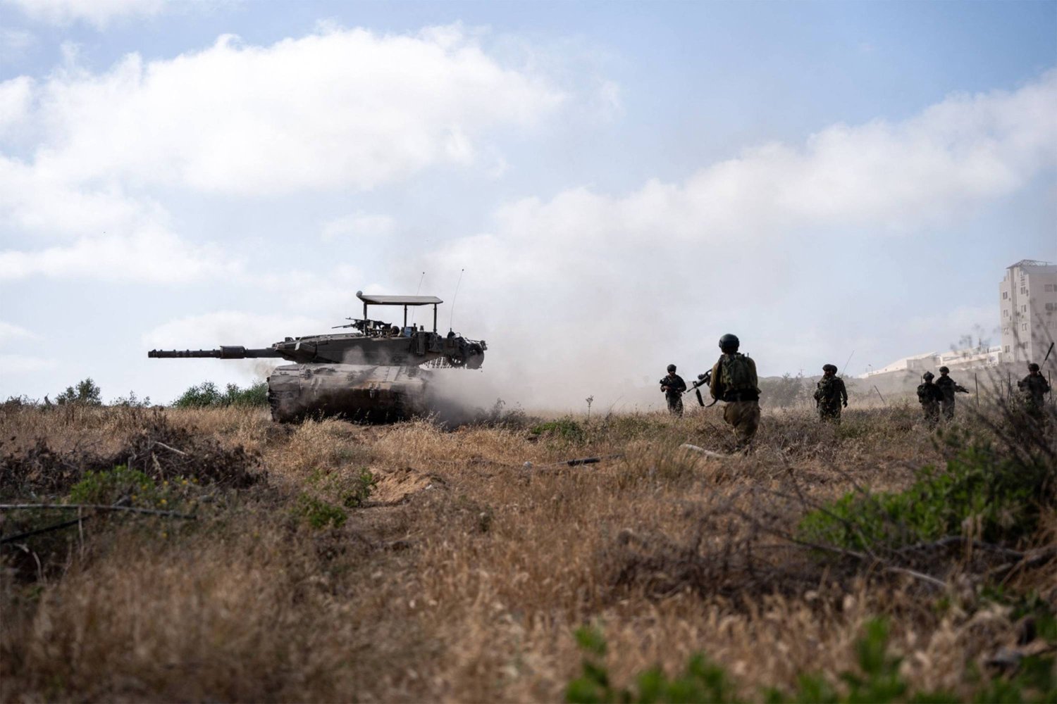 صورة نشرها الجيش الإسرائيلي في 10 مايو تظهر جنودا إسرائيليين يسيرون بجوار دبابة قتال رئيسية كجزء من نشاط الفرقة 99 في منطقة الزيتون بمدينة غزة (أ.ف.ب)