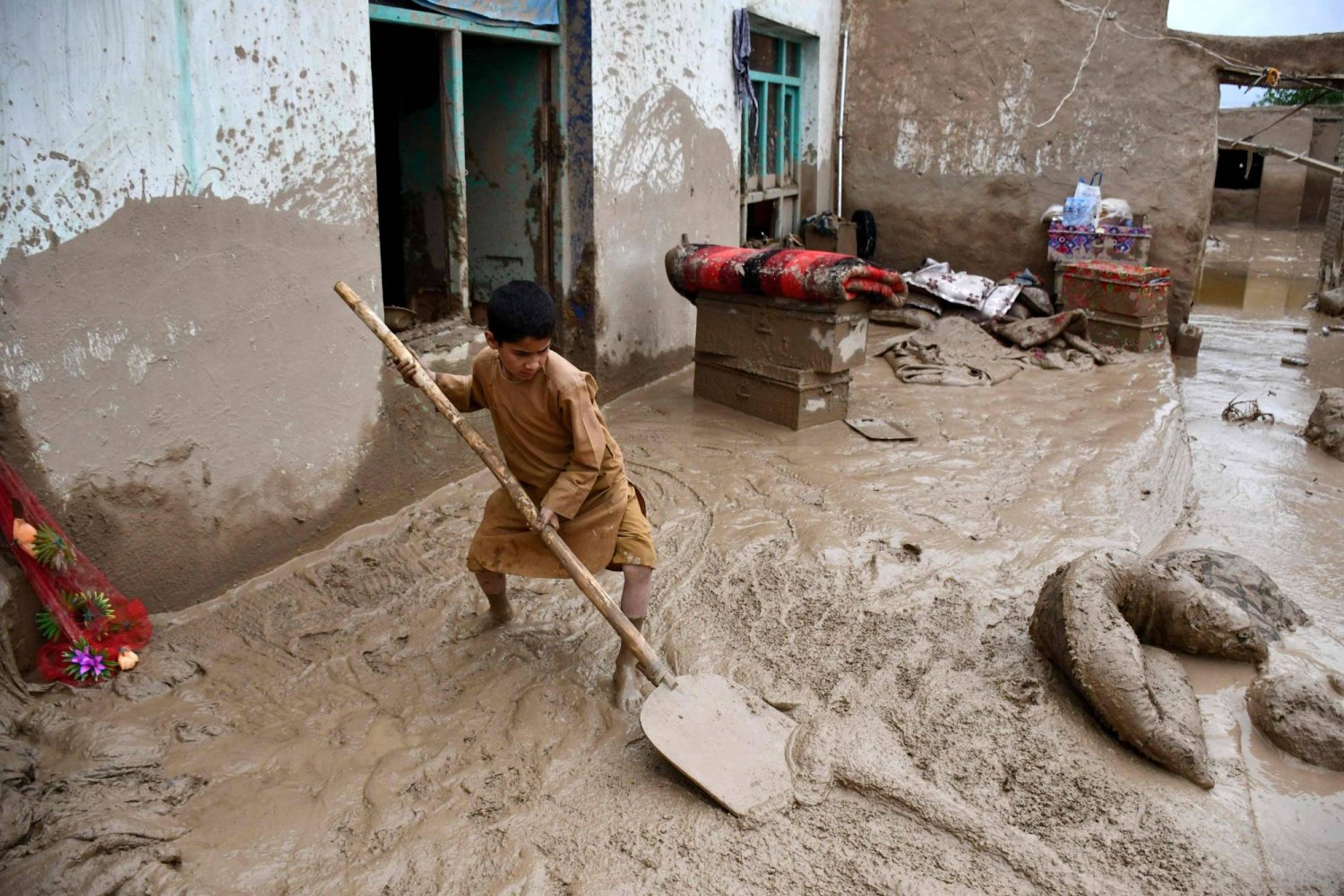 شاب أفغاني يزيح الطين من خارج بيته في بغلان، في 11 مايو (أ.ف.ب)