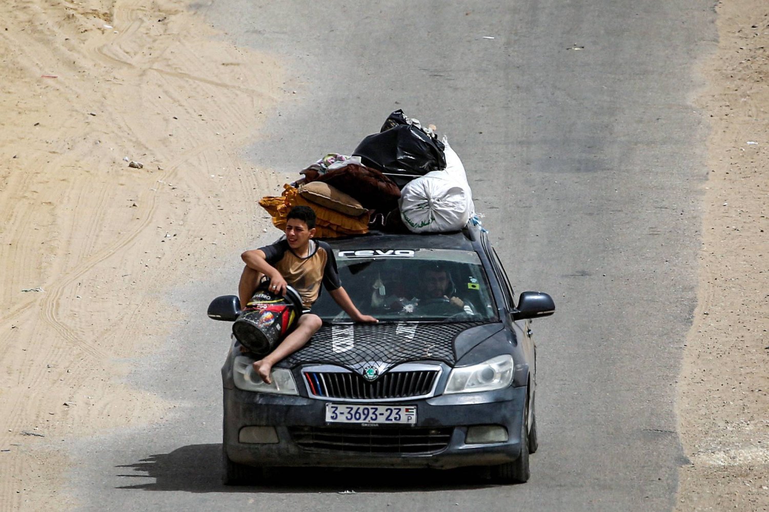 Filistinli bir aile Han Yunus'a doğru giderken arabanın kaputunda oturan bir çocuk (AFP)