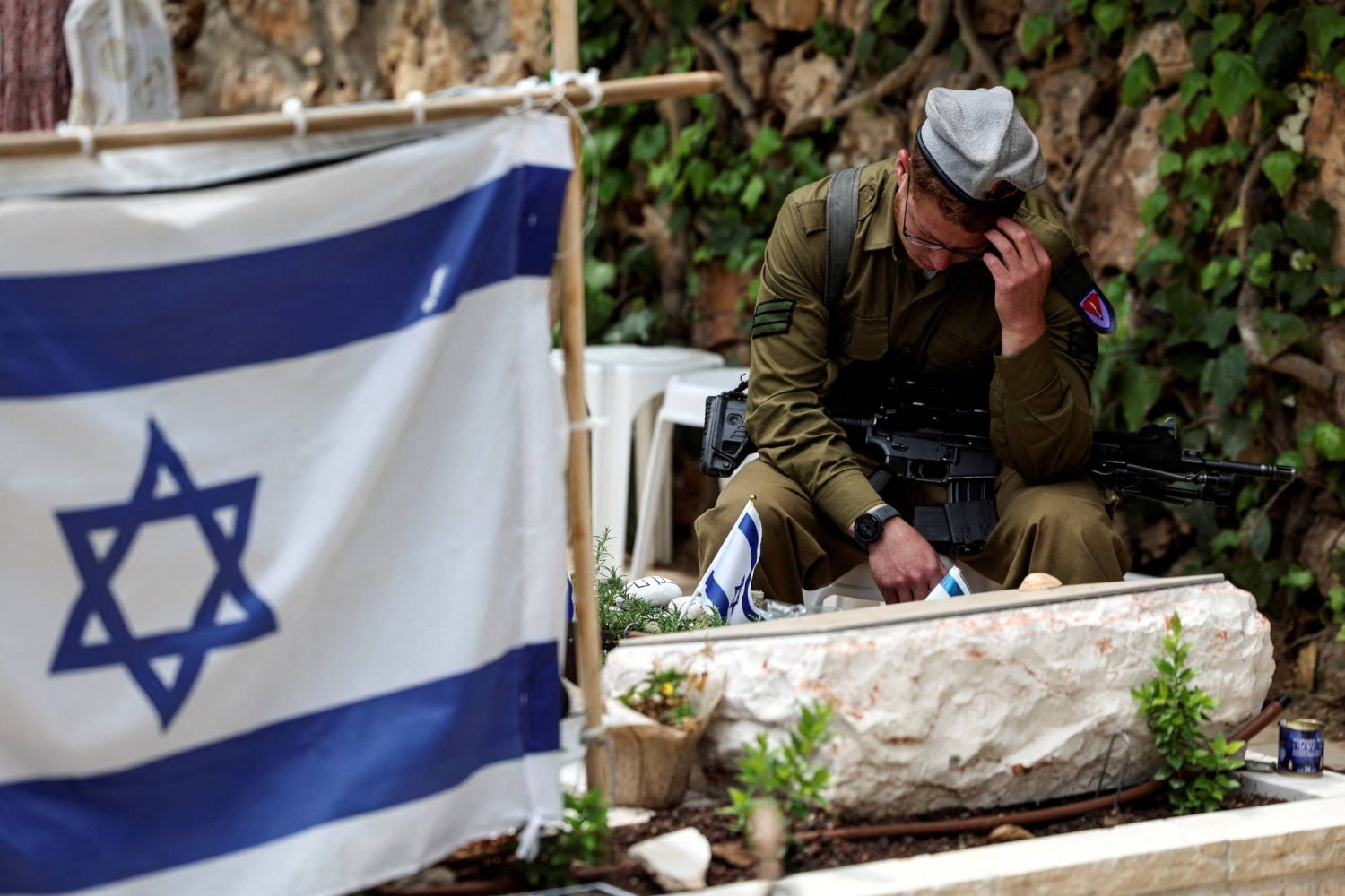 جندي يجلس في القدس يوم الأحد إلى جوار مقبرة زميل له قُتل في غزة (رويترز)