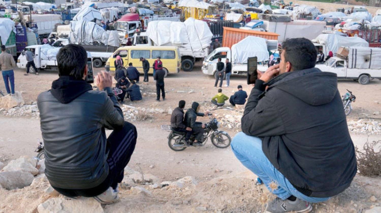 لاجئان سوريان قررا البقاء في لبنان يصوّران قافلةً من السوريين العائدين إلى بلادهم في منطقة عرسال الحدودية يوم 26 أكتوبر الماضي (أ.ب)