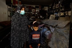 امرأة فلسطينية وطفلها يقفان في وسط الدمار الذي خلفه القصف الإسرائيلي على منزل في رفح (رويترز)