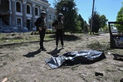 ضباط أوكرانيون يقفون بجوار جثة بعد غارة استهدفت قرية في منطقة خاركيف (أ.ف.ب)