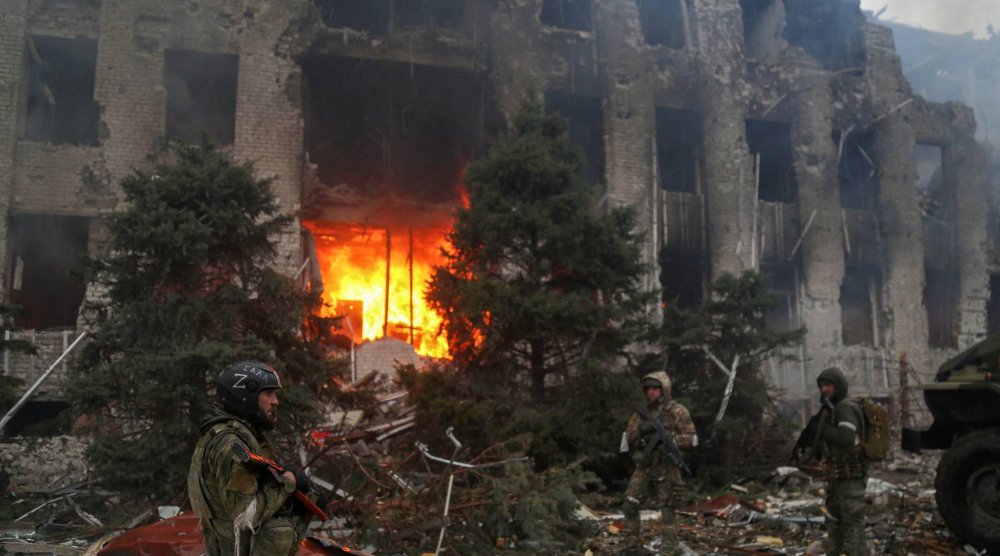 قوات موالية لروسيا تقف أمام مبنى مدمر في أوكرانيا (رويترز)