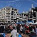فلسطينيون في سوق أقيم في الهواء الطلق قرب أنقاض المباني التي دمرتها الضربات الإسرائيلية وسط هدنة مؤقتة في مخيم النصيرات بقطاع غزة الخميس (رويترز)