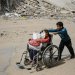 فتى فلسطيني يدفع طفلة على كرسي متحرك وسط الدمار في غزة (أ.ف.ب)