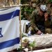جندي يجلس في القدس يوم الأحد إلى جوار مقبرة زميل له قُتل في غزة (رويترز)